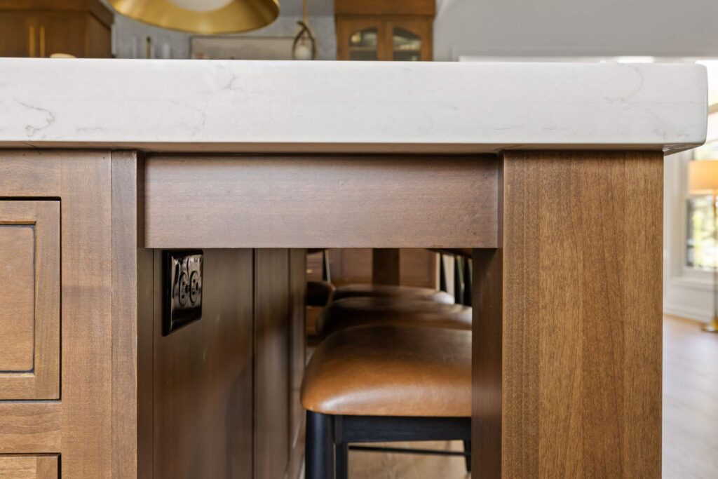Thick quartz countertop edge above a wood kitchen island leg, with a stool tucked beneath the overhang.