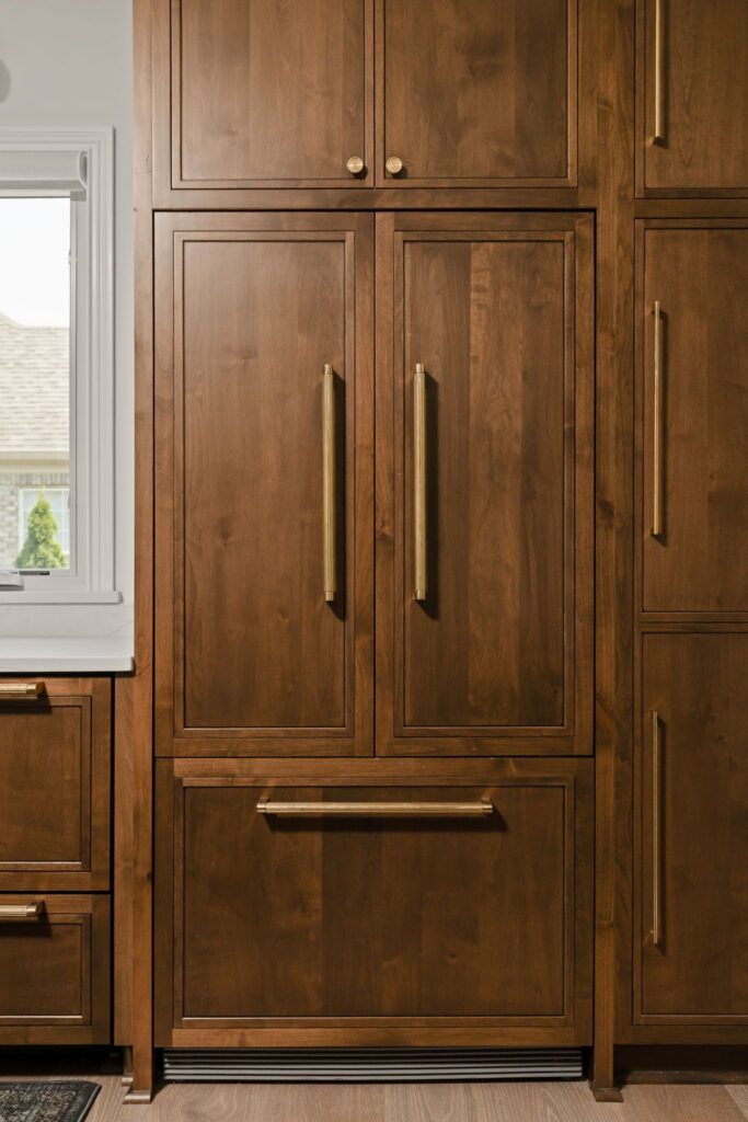 Paneled French door refrigerator with a lower freezer drawer, matching wood cabinetry and bronze-toned handles.