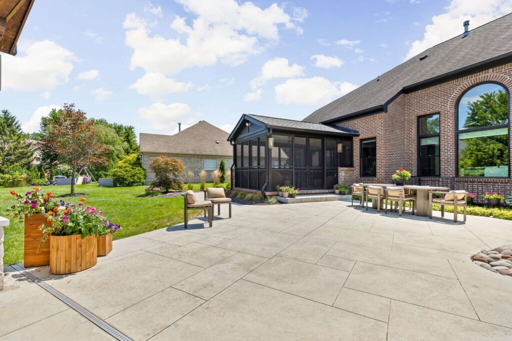 Large concrete patio with a rectangular cut pattern and outdoor dining beside the brick Carmel home.