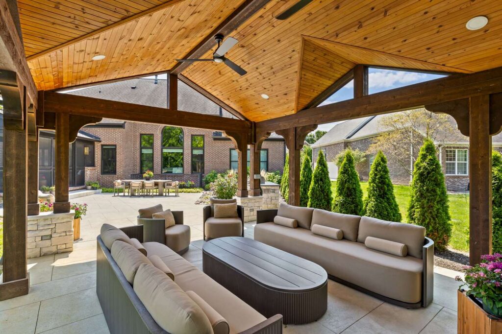 Vaulted pine ceiling and dark wood posts above pavilion seating, with the Carmel home visible beyond.