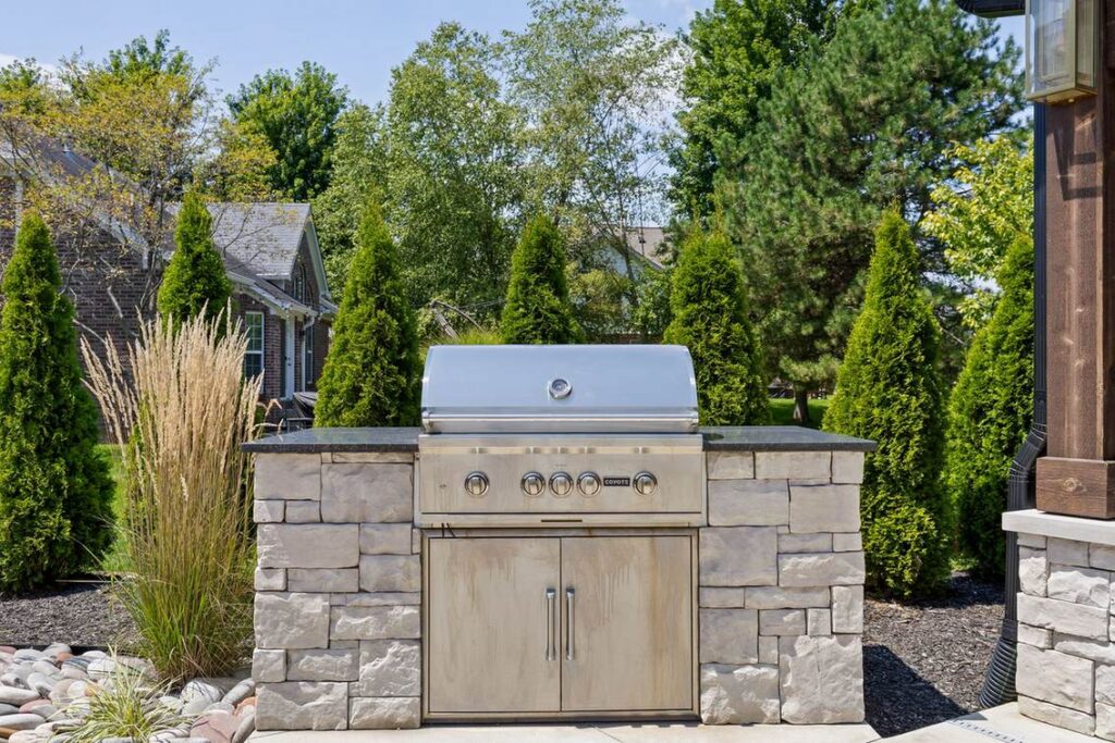 Coyote gas grill set into a stone island with a dark granite countertop and stainless steel access doors.