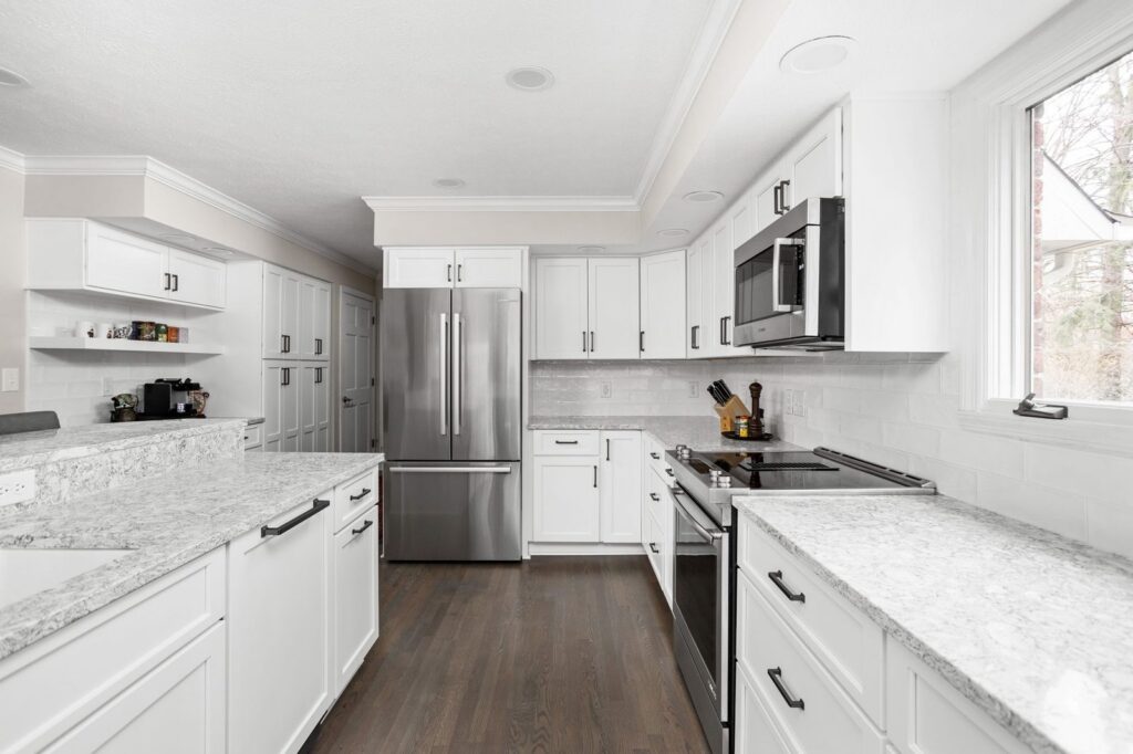 White kitchen cabinets with light quartz countertops, black hardware and stainless appliances.