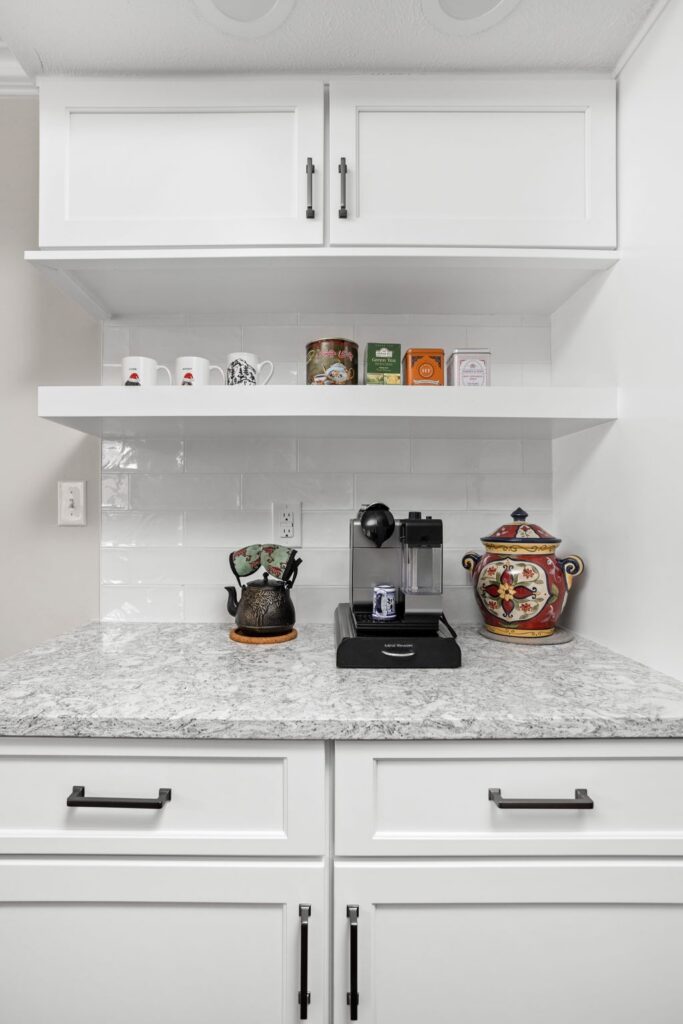 White floating kitchen shelf above a coffee station with white cabinetry and a light stone countertop.