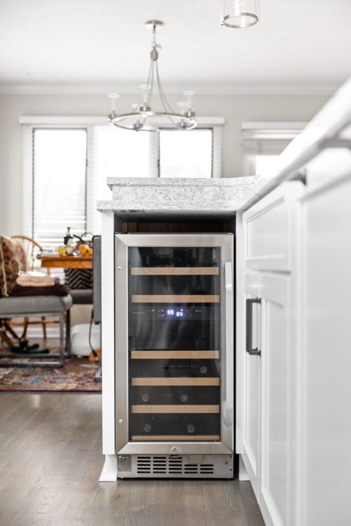 Undercounter beverage refrigerator built into the end of a light stone kitchen island.