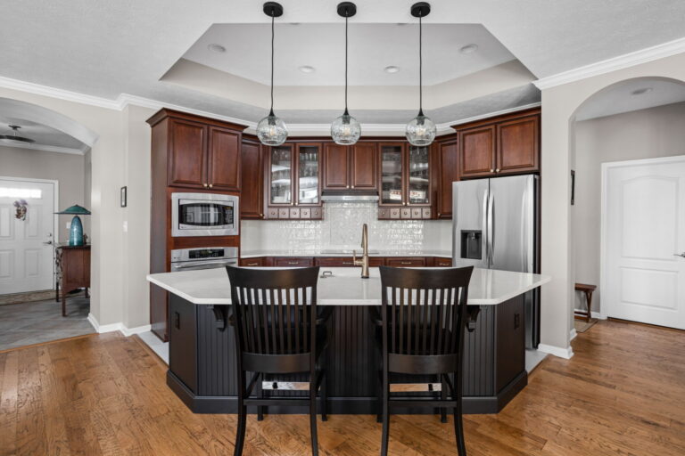 Front view of the finished Westfield kitchen with a Tricorn Black island, quartz countertop, stained cabinetry and three glass pendants.