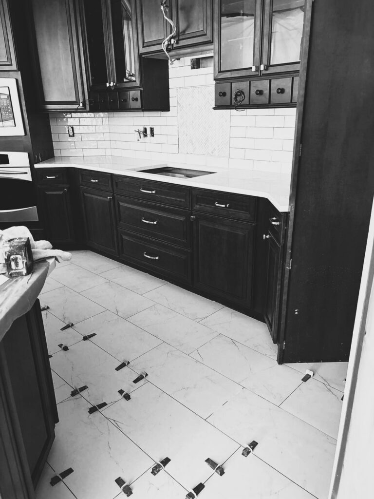 During the Westfield kitchen makeover, new large-format floor tile and white countertops were being installed around the retained stained cabinetry.