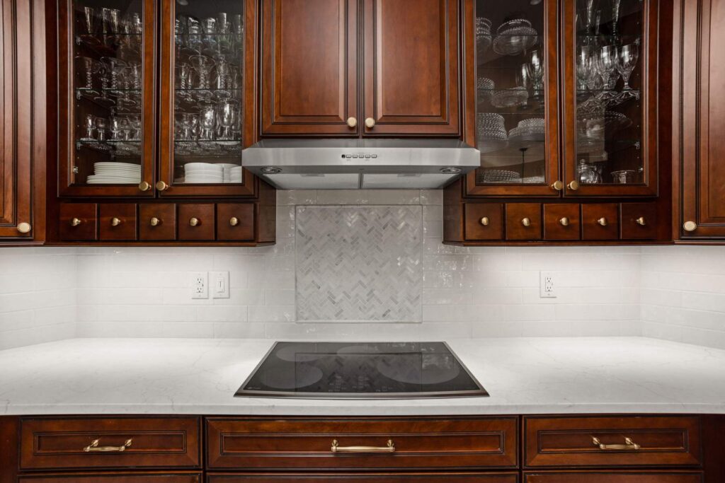 Westfield kitchen cooktop wall with stained glass-front cabinetry, white subway tile and marble herringbone backsplash accent.