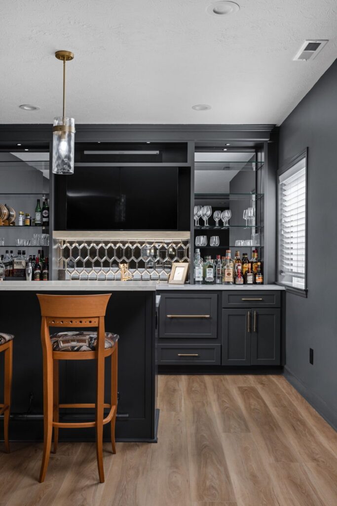 Basement wet bar in Noblesville with raised seating, dark cabinets, mirrored display shelves and a built-in television.