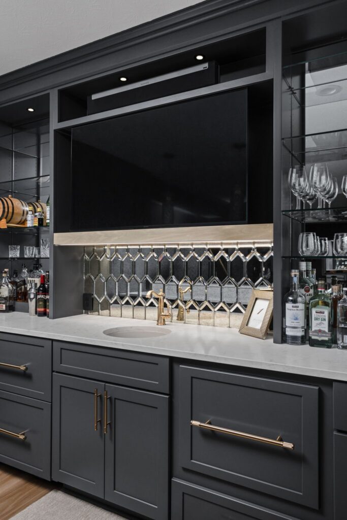 Noblesville basement wet bar with dark cabinetry, a round sink, mirrored hexagon backsplash and glass display shelves.