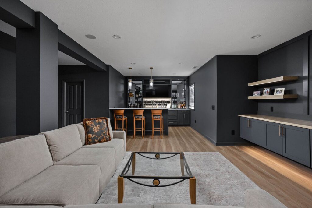 Finished basement in Noblesville with a wet bar, raised seating, floating cabinets and wood shelves beside the lounge area.