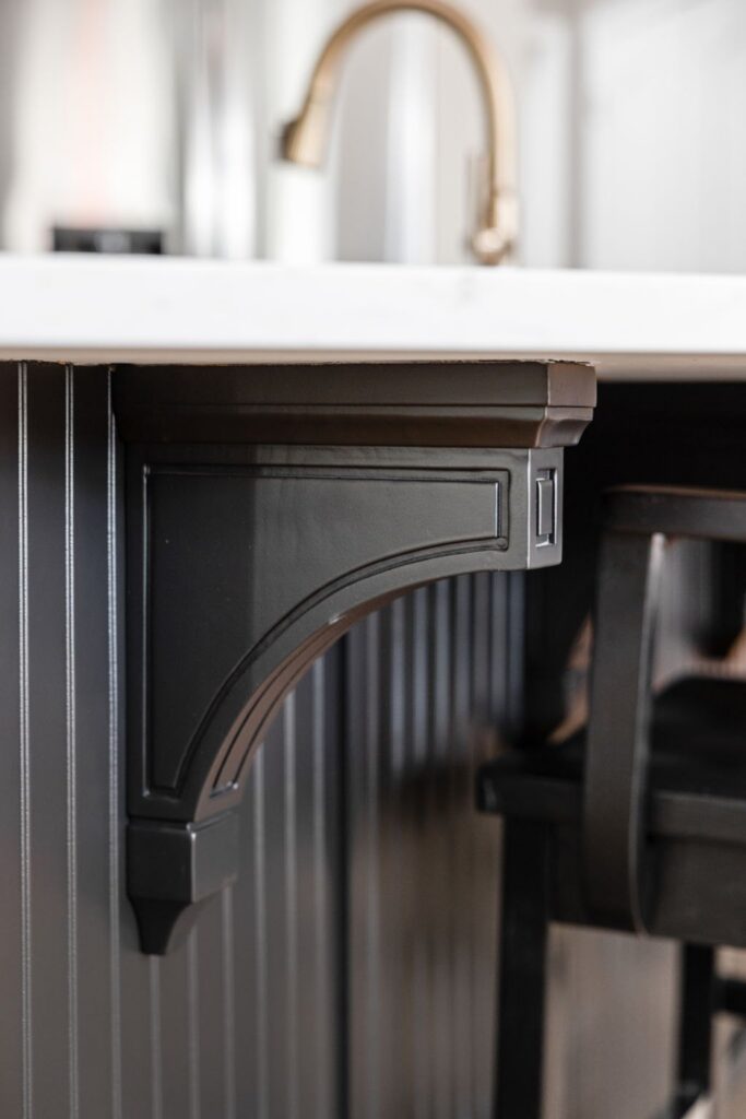 Close-up of the black kitchen island corbel and beadboard-style panel beneath the white quartz countertop.