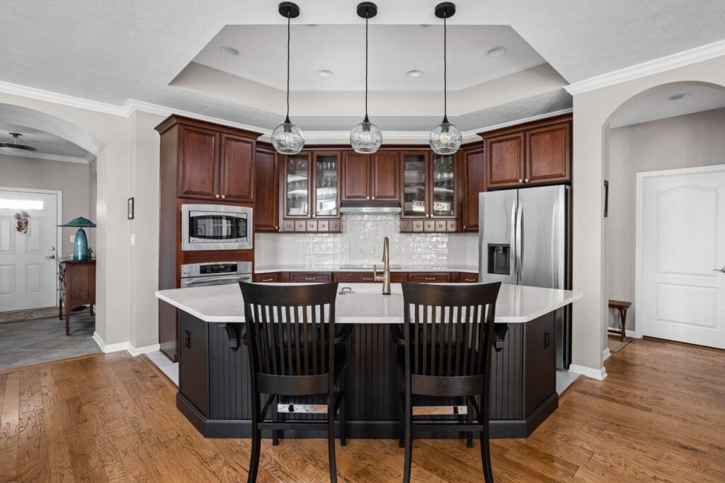 Front view of the finished Westfield kitchen with a Tricorn Black island, quartz countertop, stained cabinetry and three glass pendants.
