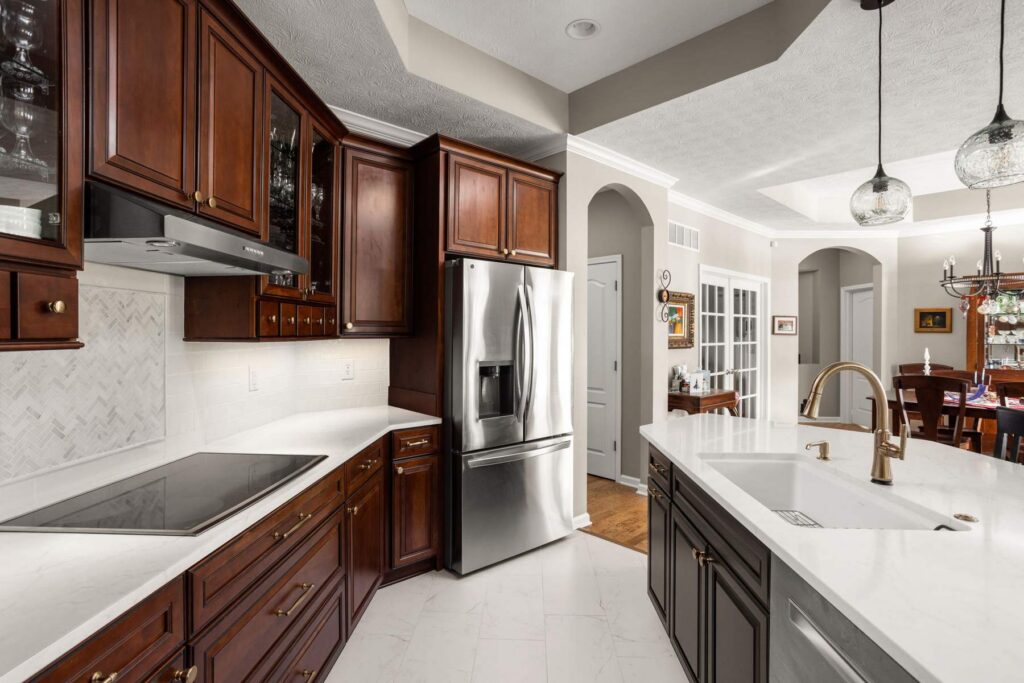 Finished Westfield kitchen with stained perimeter cabinetry, white quartz countertops, stainless steel refrigerator and contrasting black island.